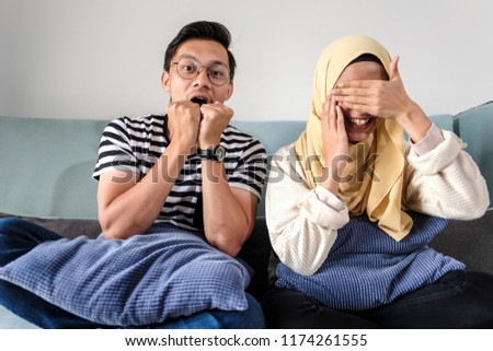 Muslim couple enjoying while watching horror tv on a couch at home
