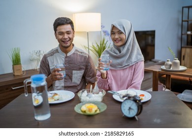 Muslim Couple Wake Up Early To Have Sahur Or Suhur Breakfast For Fasting. Clock At Foreground Showing The Time