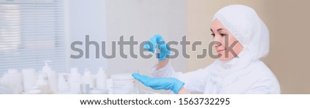 Muslim doctor cosmetologist holds in her hands a pipette with a cosmetology product. Long banner for website design. Photos in the interior of the clinic. Copy space.