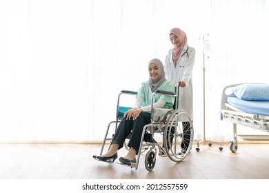 Muslim doctor pushing of a female patient sitting on wheelchair in a hospital. Joyful physician taking care of and assisting a sick person in clinic. Insurance, Medical, Patient care process concepts