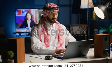 Muslim entrepreneur working from home, using laptop and writing notes. Middle Eastern man in personal apartment office answering emails and transcribing important info on notepad