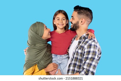 Muslim Family Embracing Posing Together On Blue Background. Studio Shot Of Happy Middle Eastern Parents Holding And Hugging Little Daughter Smiling To Camera. - Shutterstock ID 2151888321