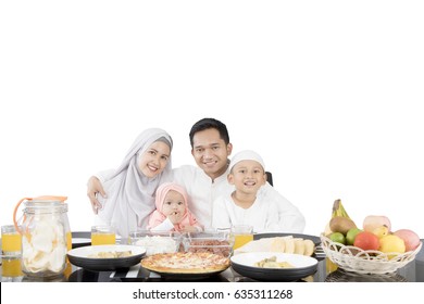 Muslim Family Having Meal At Dining Table While Smiling At The Camera, Isolated On White Background 