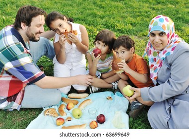 Muslim Family, Mother And Father With Three Children Together In Nature Sitting And Eating On Green Grass: Picnic