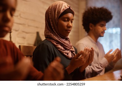 Muslim family praying before a meal at dining table. Focus is on mother. - Powered by Shutterstock