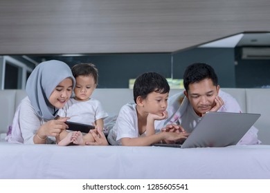 Muslim Family Using A Laptop And Mobile Phone While Lying Together On The Bed