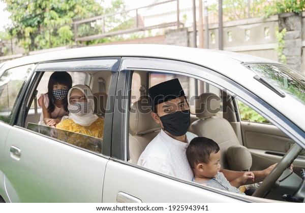 Muslim family wearing face mask during travel by\
car on eid mubarak celebration. asian people going back to their\
hometown