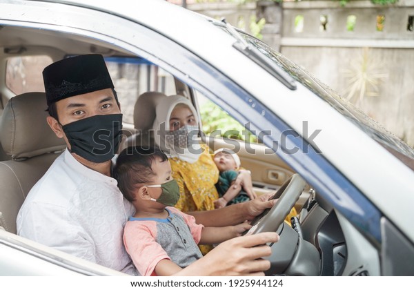 Muslim family wearing face mask during travel by\
car on eid mubarak celebration. asian people going back to their\
hometown