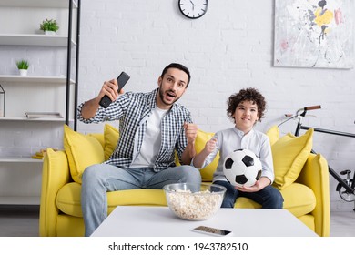 Muslim father and son with football watching match near popcorn at home - Powered by Shutterstock