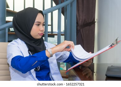 Muslim Female Doctor Review Medical Report In A Clinic With A Serious And Focus Face Expression.