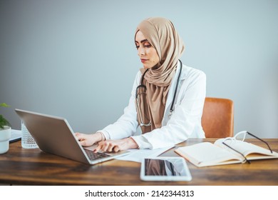 A Muslim Female Doctor Is Sitting At The Table At Home And Working On Her Laptop. A Happy And Confident Muslim Woman Is Using Her Laptop In Her Living Room.