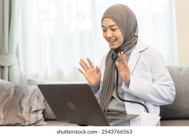 Muslim female doctor wearing hijab smiling and using laptop holding stethoscope, offering online medical consultation, remote healthcare services and telemedicine support in a modern medical setting - Powered by Shutterstock