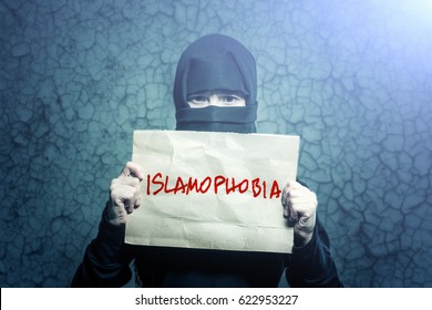 Muslim girl in black hijab holding a poster with an inscription ISLAMOPHOBIA against a wall with cracks