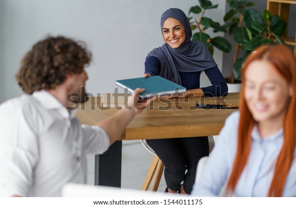 Muslim girl doing a favor and giving a book to\
her fellow university student he needs a lot. Muslim and Christian\
people coexist.
