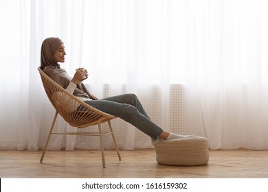 Muslim Girl In Hijab Relaxing In Chair With Coffee, Enjoying Weekend, Sitting Against Window At Home, Copy Space - Powered by Shutterstock