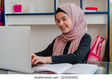 Muslim Girl Student In Hijab Smiling While Learning For School At Home Desk Using A Laptop.	