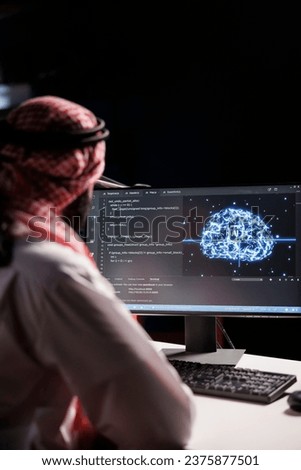 Muslim guy working with code and AI interface on a desktop computer. He is a professional developer managing data on a networked server in a cloud-based data center.