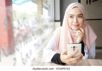 Muslim Hijab Women Holding A Phone While Looking Out The Window. Thinking Of Good Memories. 