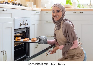 Muslim Housewife. Portrait Of Smiling Woman In Hijab Baking In Kitchen, Cheerful Islamic Lady Wearing Apron And Mitten, Taking Tray With Homemade Muffins Out Of Hot Oven, Free Space - Powered by Shutterstock