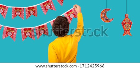 Muslim Kid preparing decorations to celebrate Ramadan festival - lantern , crescent , and paper Islamic shapes with word Ramadan Kareem - Translation : Ramadan is generous