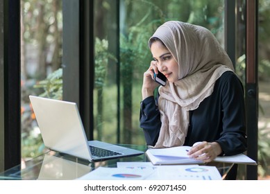 Muslim lady is busy on the phone at her desk.