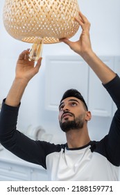 Muslim Man Holding Lightbulb Near Chandelier In Kitchen