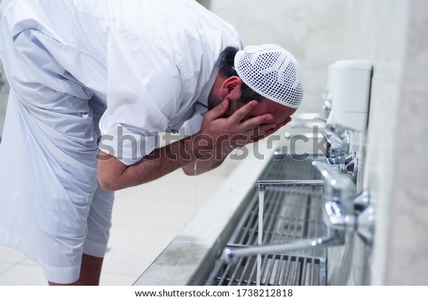 Muslim man taking ablution for prayer. Islamic\
Religious Rite Ceremony Of Ablution. Young Muslim man perform\
ablution (wudhu) before\
prayer.