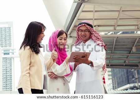 Muslim man and woman is looking at tablet with smart lady is standing beside in city.