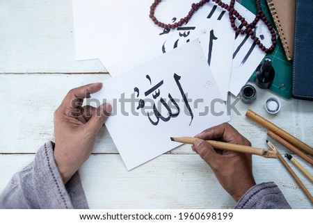 Muslim man writing Khat with bamboo pen on paper, Arabic letters mean the name of Muslim god 