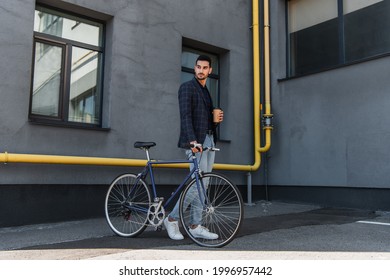 Muslim manager with paper cup and bicycle walking near building