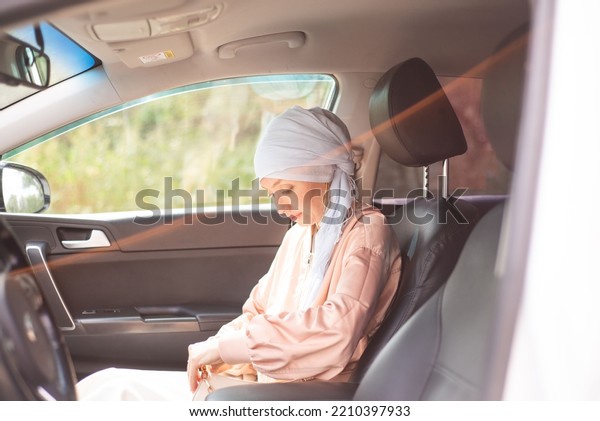 Muslim\
modern woman is sitting in car and looking at\
bag.