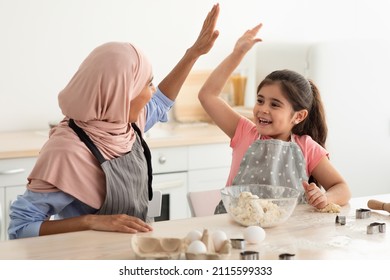 Muslim Mom And Daughter Giving High Five To Each Other While Baking Cake In Kitchen, Happy Islamic Mother In Hijab Cooking Pastry With Her Cute Little Female Child, Bonding Together At Home, Closeup