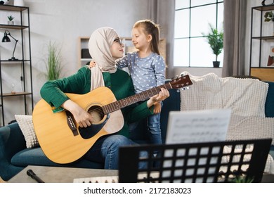 Muslim Mom And Little Happy Girl In Music Therapy By Playing Guitar On Music Room. Teacher Helping Young Female Pupil In Guitar Lesson. Relaxing At Home.