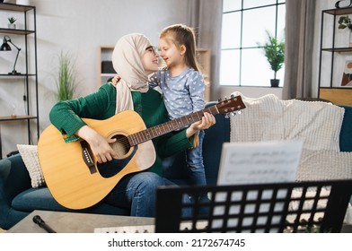 Muslim Mom And Little Happy Girl In Music Therapy By Playing Guitar On Music Room. Teacher Helping Young Female Pupil In Guitar Lesson. Relaxing At Home.