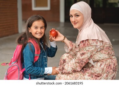 Muslim mother and the happy kid girl getting ready for the first school day. Loving Muslim Mom Helping Her Daughter packing apple and lunch for break meal. A female parent prepares child for school.