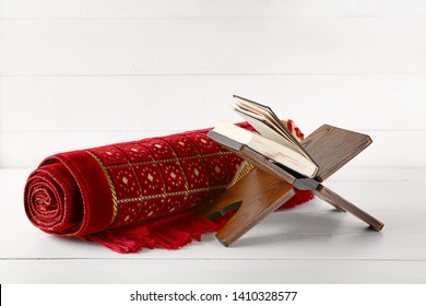 Muslim Prayer Mat And Koran On White Wooden Table