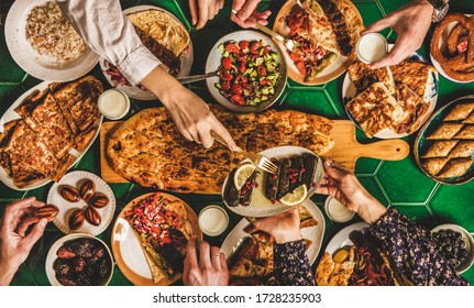 Muslim Ramadan iftar family dinner. Flat-lay of people feasting over table with Middle East food. Dates, dolma, kebab, flatbread, pide, borek, sweet, salad, top view. Ramazan fasting Turkish cuisine