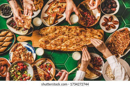 Muslim Ramadan Iftar Family Dinner. Flat-lay Of People Eating Over Middle East Food Table. Dates, Dolma, Kebab, Flatbread, Pide, Borek, Sweets, Ayran Drink, Top View. Ramazan Fasting Turkish Cuisine