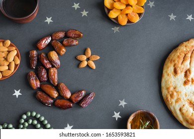 Muslim Ramadan Kareem With Dates Fruits Arranged In Shape Of Crescent Moon, Water And Bread On Black Background, Top View. Iftar Food Or Iftar Party Concept.