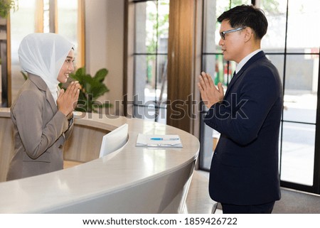 A Muslim receptionist introduces a polite greeting to the hotel guests.