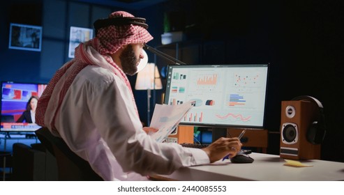 Muslim teleworker crosschecking analytics statistical data set with paperwork while remotely working in apartment office. Middle Eastern manager optimizing key performance indicators