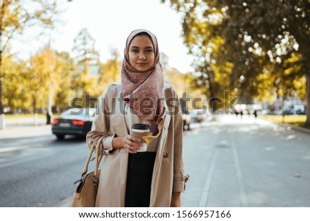 muslim woman in business clothes and a scarf with coffee in hand on a city street