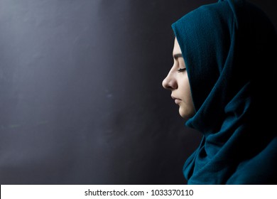 A Muslim woman with closed eyes, on a black background. Arab girl in hijab in profile.