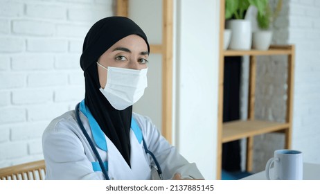 Muslim Woman Doctor In A Mask Looks At The Camera. Working In A Hospital For Women In The Arab World. A Medical Worker In A Black Veil And Medical Gown At The Workplace.