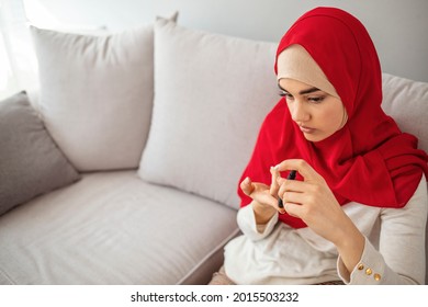 Muslim woman doing blood sugar test at home in a living room. Selective focus to her finger. Woman with glucometer checking blood sugar level at home.