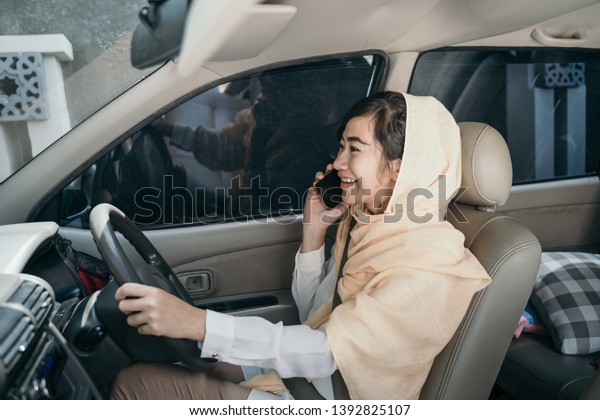 muslim woman driving car while having phone call.\
shoot from behind