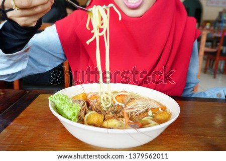 Muslim Woman enjoy eating delicious noodle or Malaysia Spicy Noodle Mee Rebus in a local restaurant.