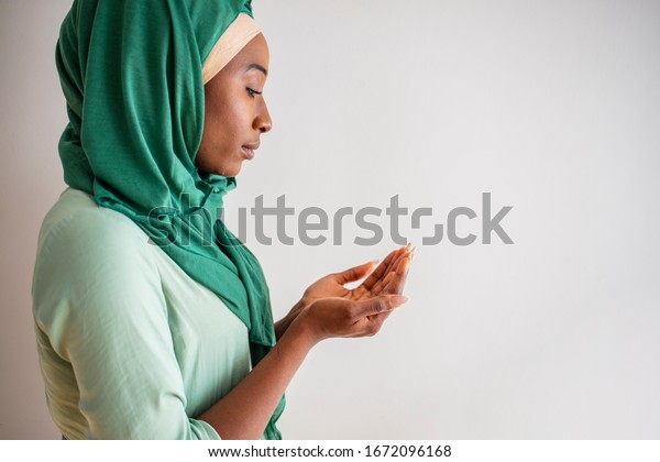 Muslim woman in green hijab and traditional clothes\
praying for Allah, copy space. Arab Muslim woman praying, isolated\
on grey background. Humble Muslim woman holding hands up and\
praying in peace