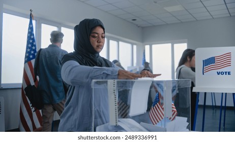 Muslim woman in hijab puts ballot paper in box. Multicultural voters, US citizens vote in voting booths at polling station. National Election Day in the United States. Democracy concept. Slow motion. - Powered by Shutterstock