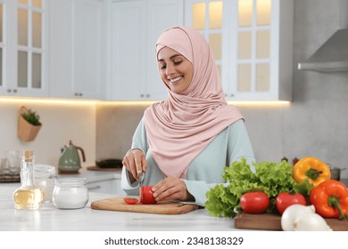 Muslim woman making delicious salad with vegetables at white table in kitchen - Powered by Shutterstock